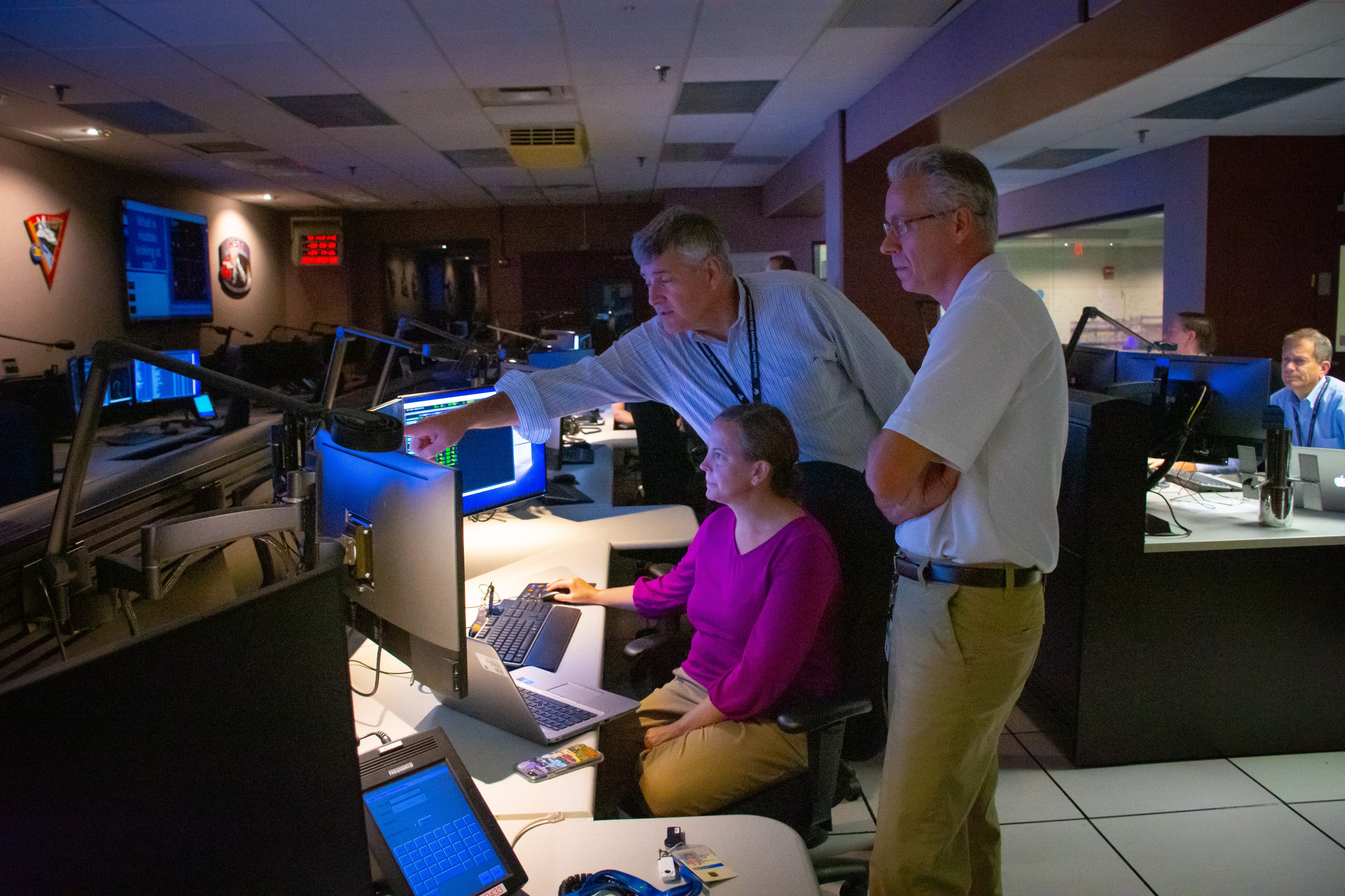 Three people discuss operations in the Hubble control center while looking at spacecraft data.