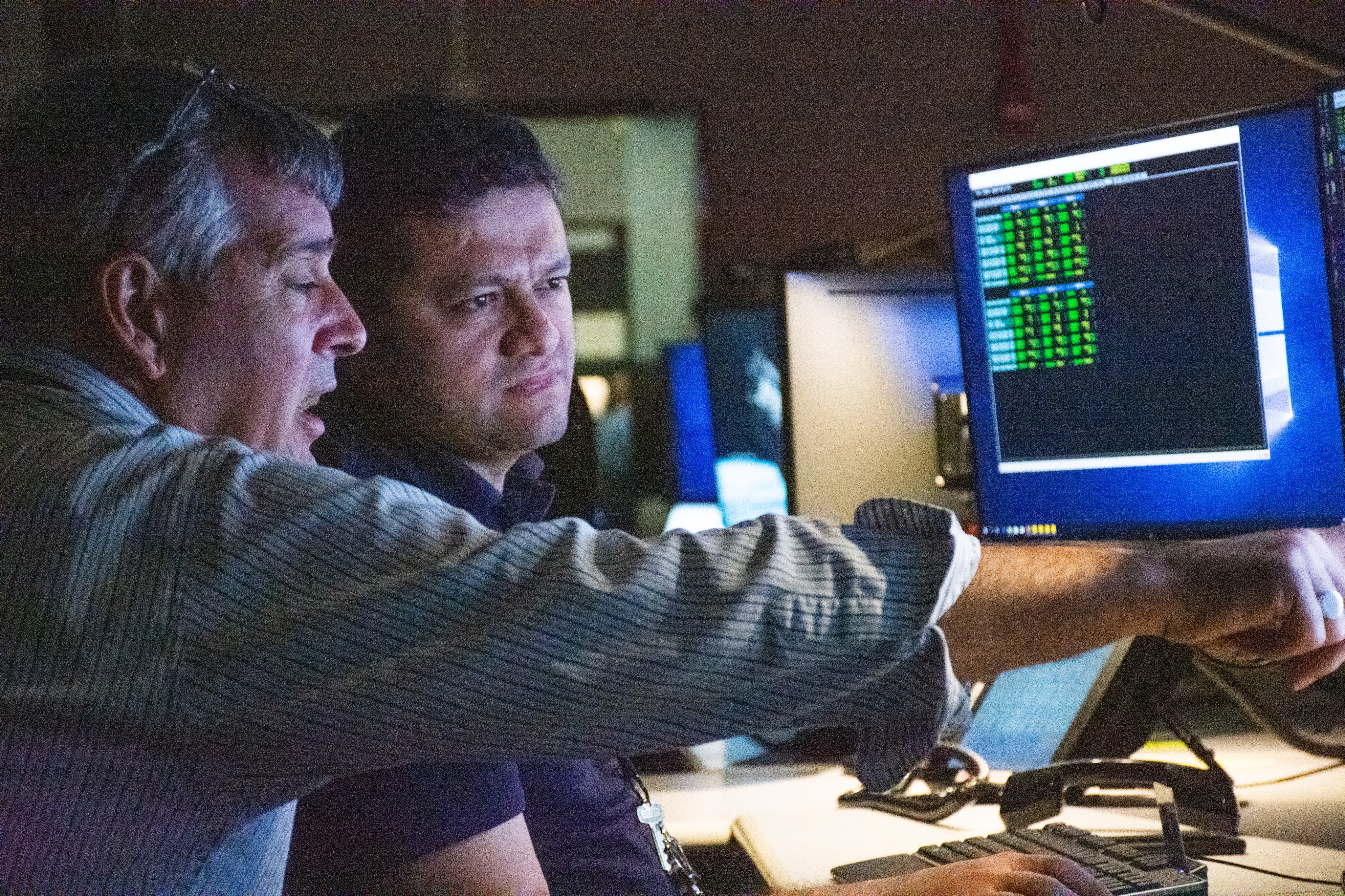 Two engineers talk about the stability of the pointing system while looking at and pointing to data on a monitor.