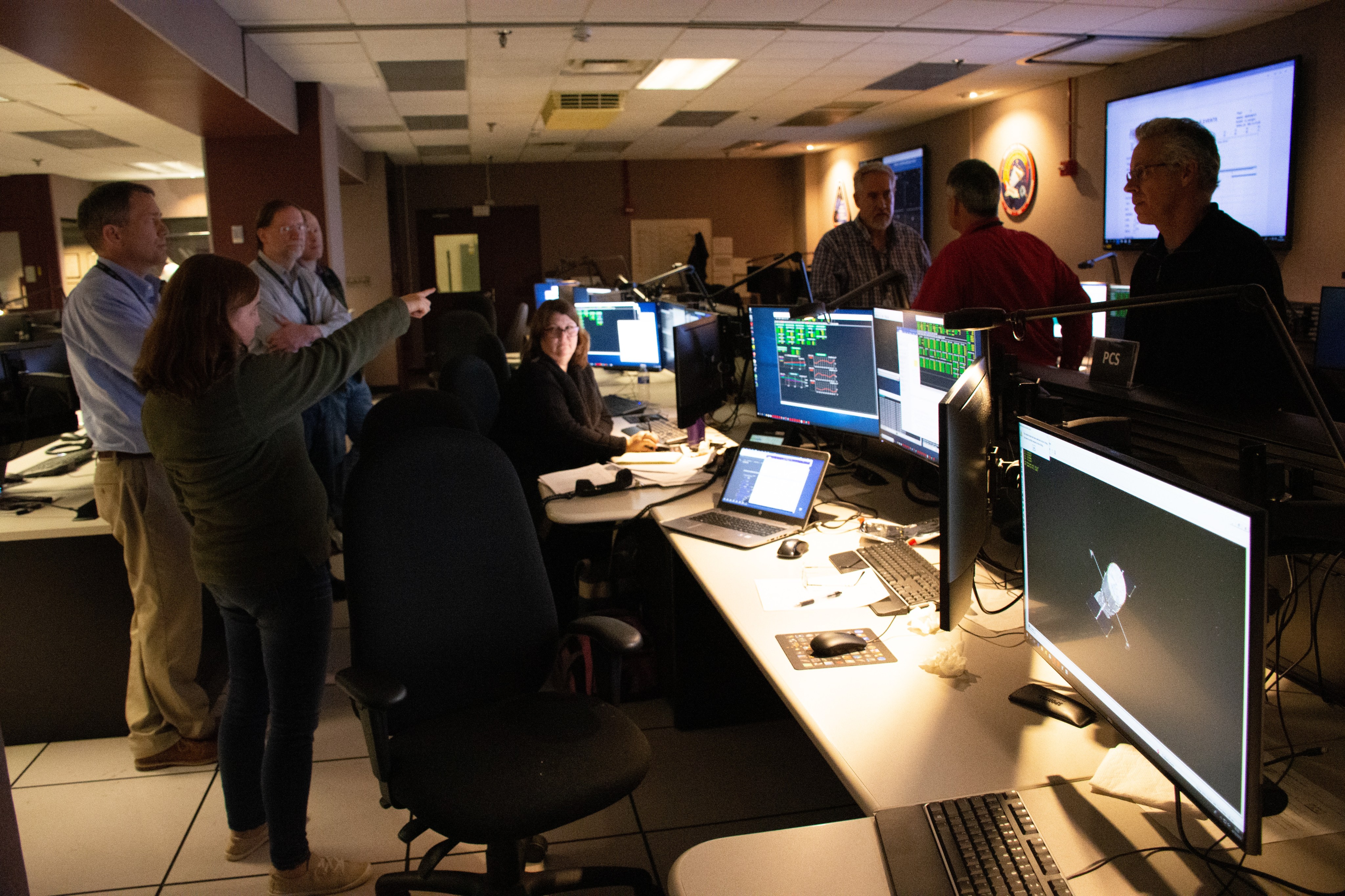 Eight people look at the data on a large screen in the Hubble operations area and discuss a test that is being conducted.