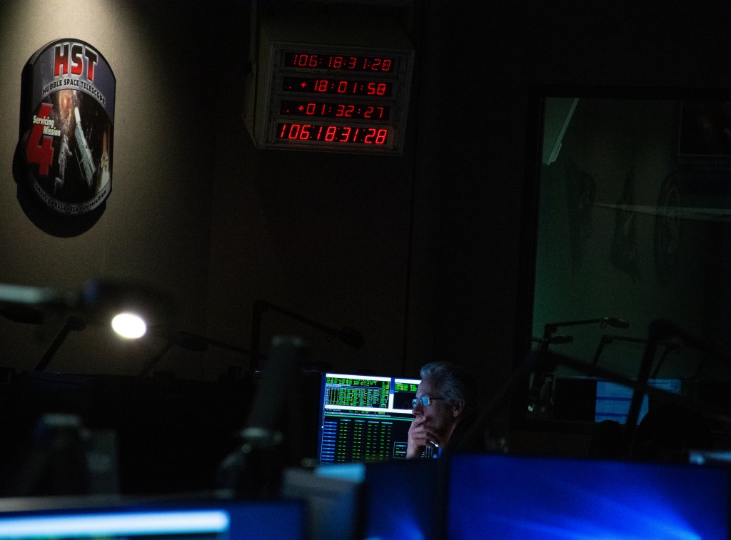 A man is pensive monitoring a Hubble operations test in the control center while looking at data on a monitor.