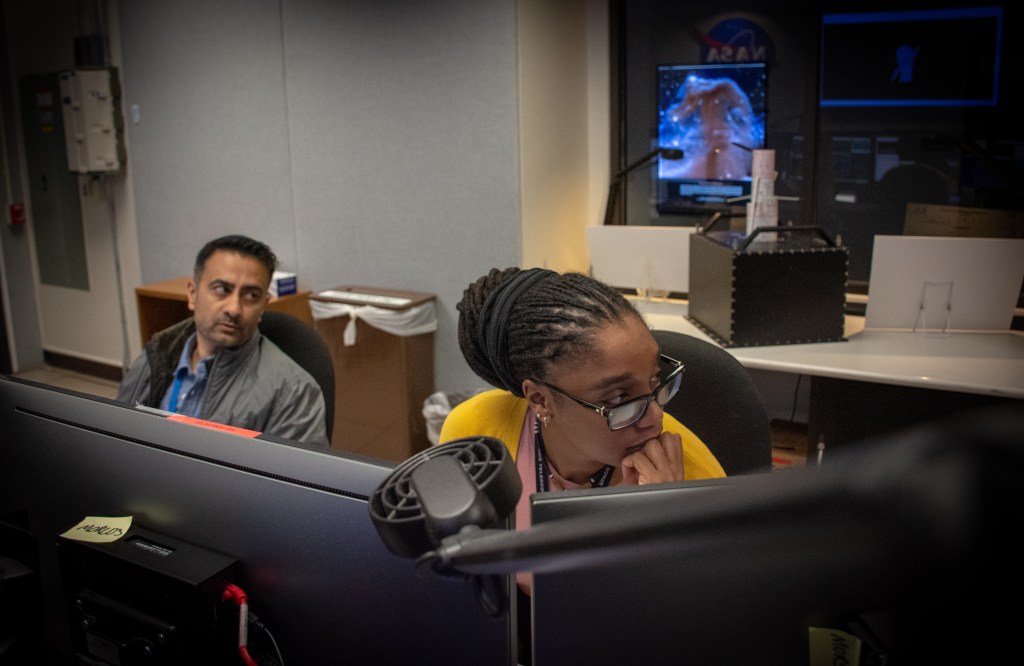 Two flight controllers look over at someone talking in the control room for Hubble.