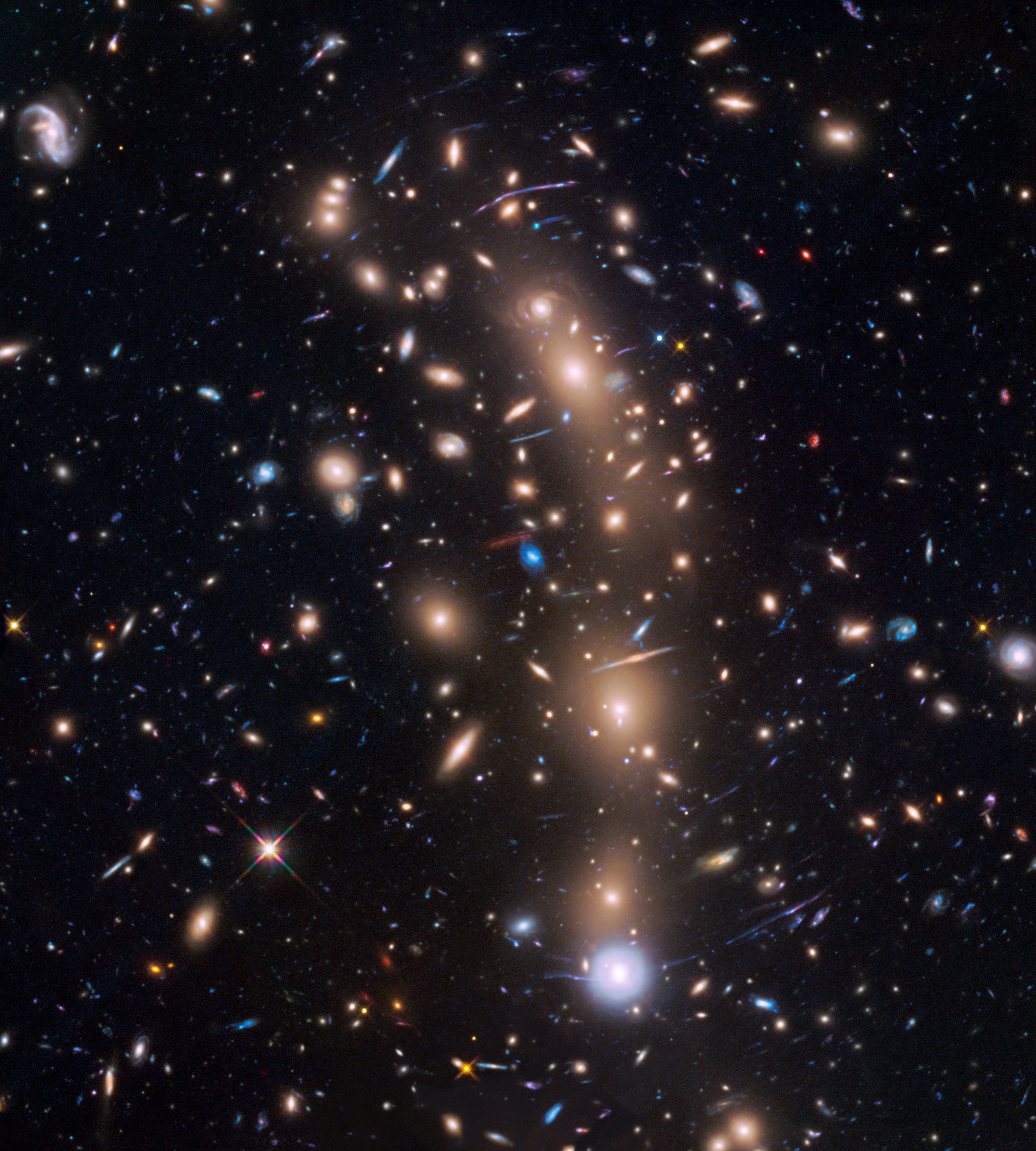 A cluster of yellow galaxies with hundreds of background galaxies. The image include arcs that are distorted images of background galaxies.