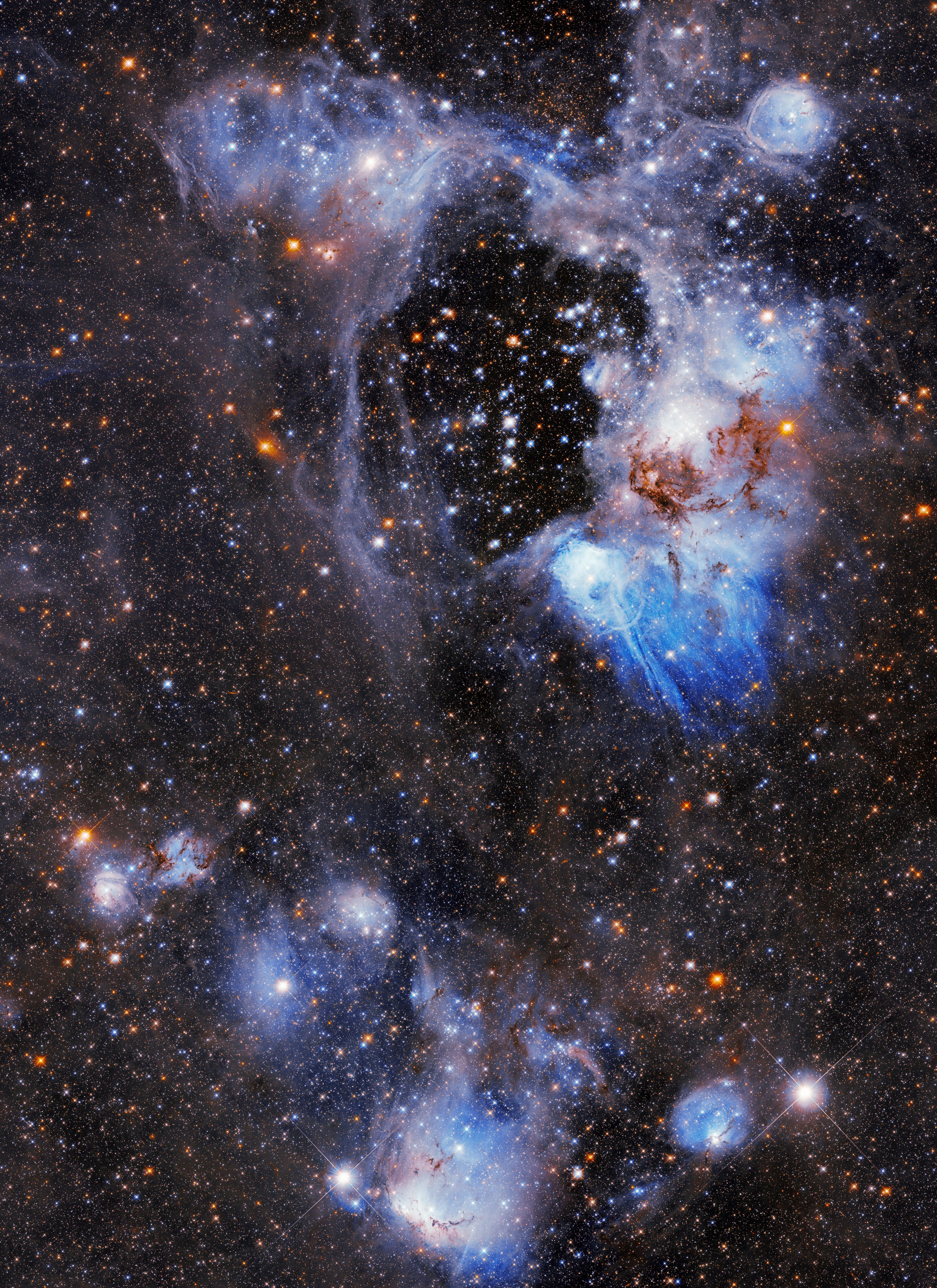 Nebula image of bright blue, purple dust surrounded by stars of all sorts of colors. At the top of the image, a large nebula with swirls and clouds of dust and gas is present, at the bottom of the image, a smaller nebula with bright white stars.