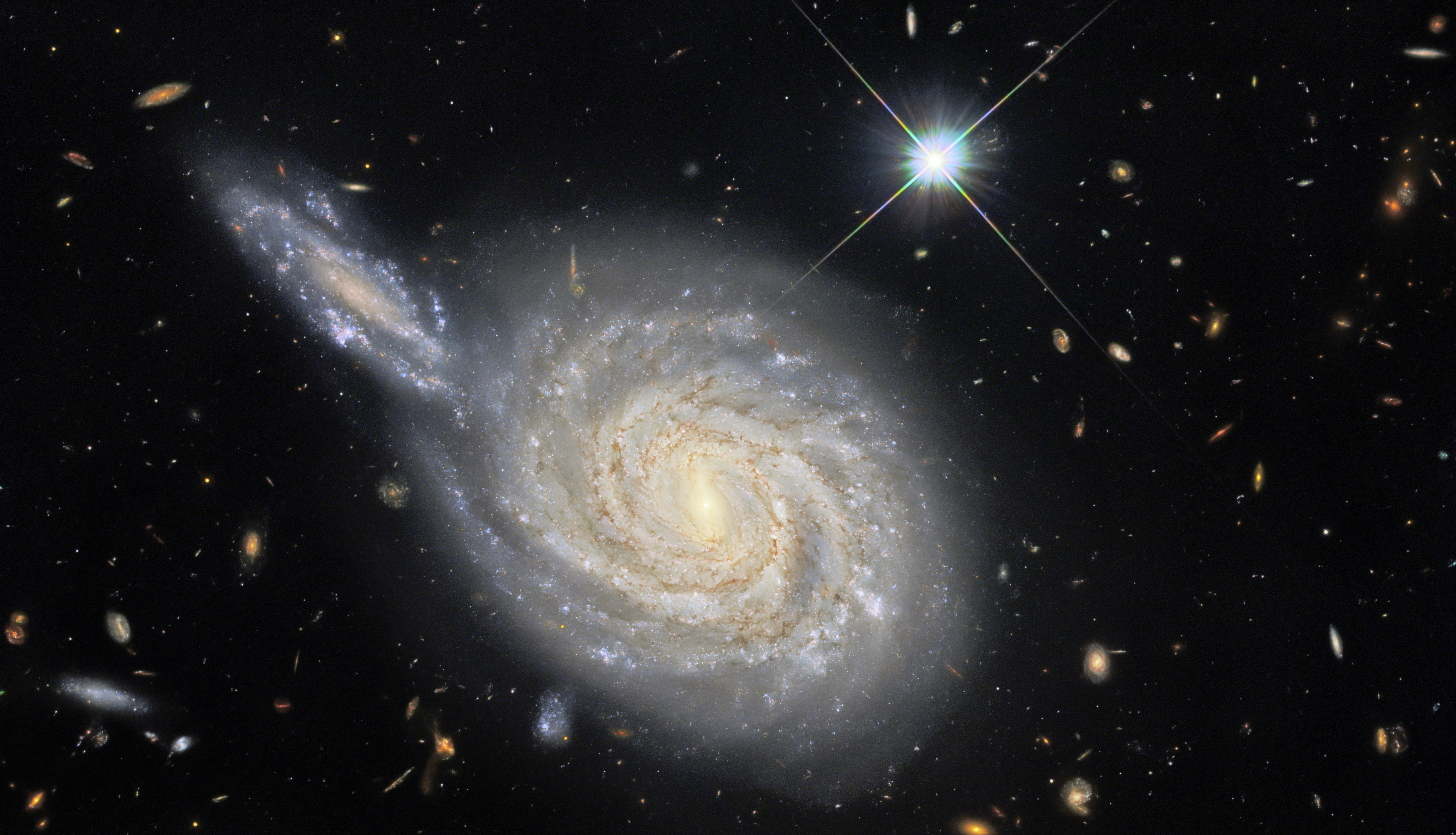 This image from the NASA/ESA Hubble Space Telescope captures the spiral galaxy NGC 105, which lies roughly 215 million light-years away in the constellation Pisces. While it looks like NGC 105 is plunging edge-on into a collision with a neighbouring galaxy, this is just the result of the chance alignment of the two objects in the night sky. NGC 105’s elongated neighbour is actually far more distant and remains relatively unknown to astronomers. These misleading conjunctions occur frequently in astronomy — for example, the stars in constellations are at vastly different distances from Earth, and only appear to form patterns thanks to the chance alignment of their component stars. The Wide Field Camera 3 observations in this image are from a vast collection of Hubble measurements examining nearby galaxies which contain two fascinating astronomical phenomena — Cepheid variables and cataclysmic supernova explosions. Whilst these two phenomena may appear to be unrelated — one is a peculiar class of pulsating stars and the other is the explosion caused by the catastrophic final throes of a massive star’s life — they are both used by astronomers for a very particular purpose: measuring the vast distances to astronomical objects. Both Cepheids and supernovae have very predictable luminosities, meaning that astronomers can tell precisely how bright they are. By measuring how bright they appear when observed from Earth, these “standard candles” can provide reliable distance measurements. NGC 105 contains both supernovae and Cepheid variables, giving astronomers a valuable opportunity to calibrate the two distance measurement techniques against one another. Astronomers recently carefully analysed the distances to a sample of galaxies including NGC 105 to measure how fast the Universe is expanding — a value known as the Hubble constant. Their results don’t agree with the predictions of the most widely-accepted cosmological model, and their analysis shows that there is only a 1-in-a-million chance that this discrepancy was caused by measurement errors. This discrepancy between galaxy measurements and cosmological predictions has been a long-standing source of consternation for astronomers, and these recent findings provide persuasive new evidence that something is either wrong or lacking in our standard model of cosmology.
