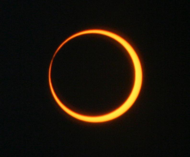 A ring of golden sunlight appears around the Moon, which looks like a black disk, set against a black background. The ring of sunlight is thinner in the upper left and thicker in the lower right.