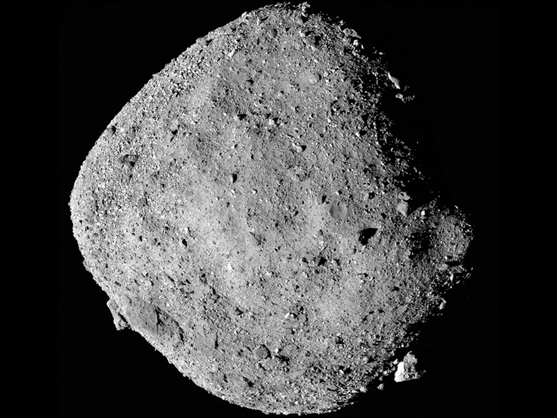 A close up view of diamond-shaped Asteroid Bennu. The asteroid appears gray in this image. Rocks and craters are visible.