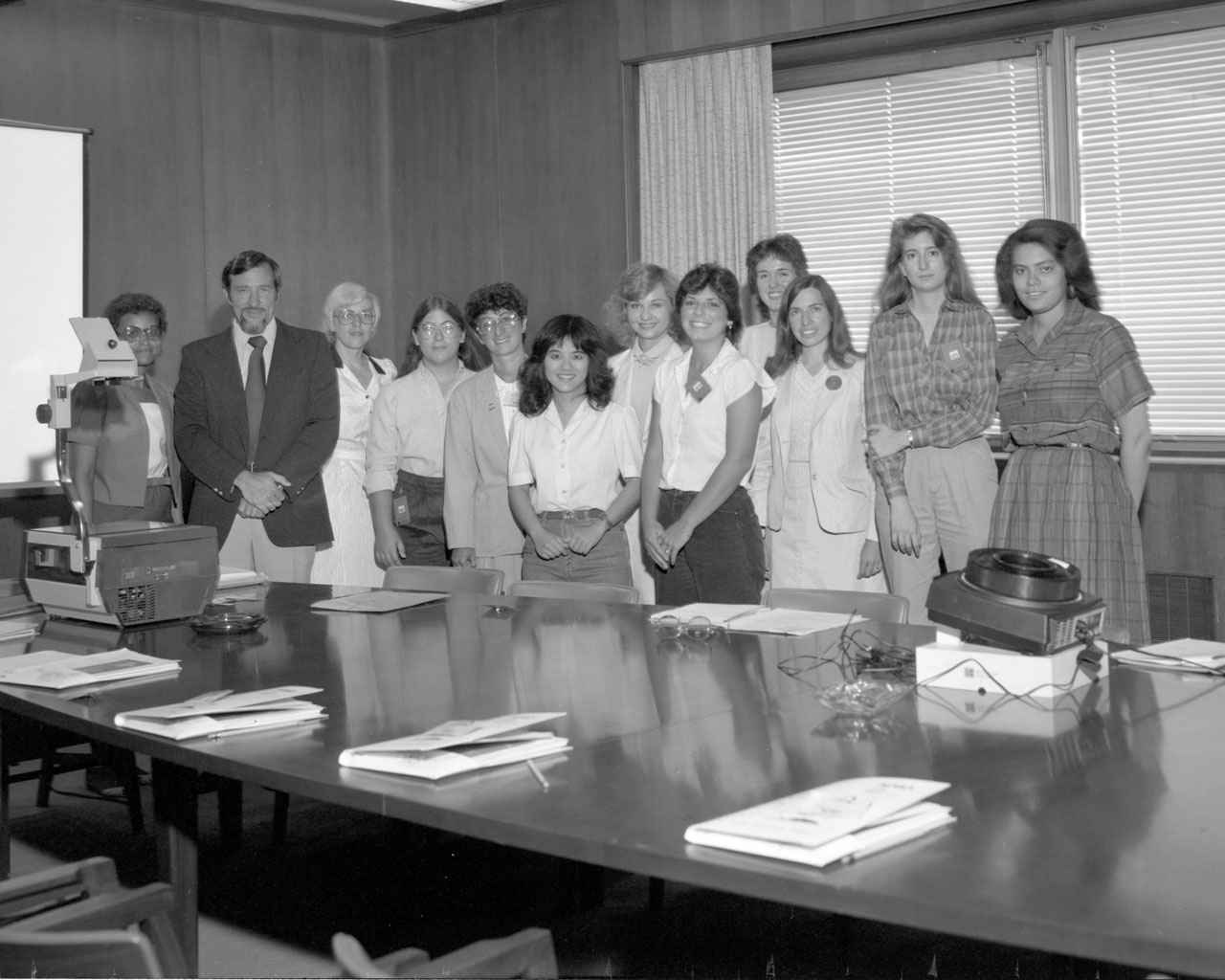 Black and white photo of group of women and one man in a NASA conference room.