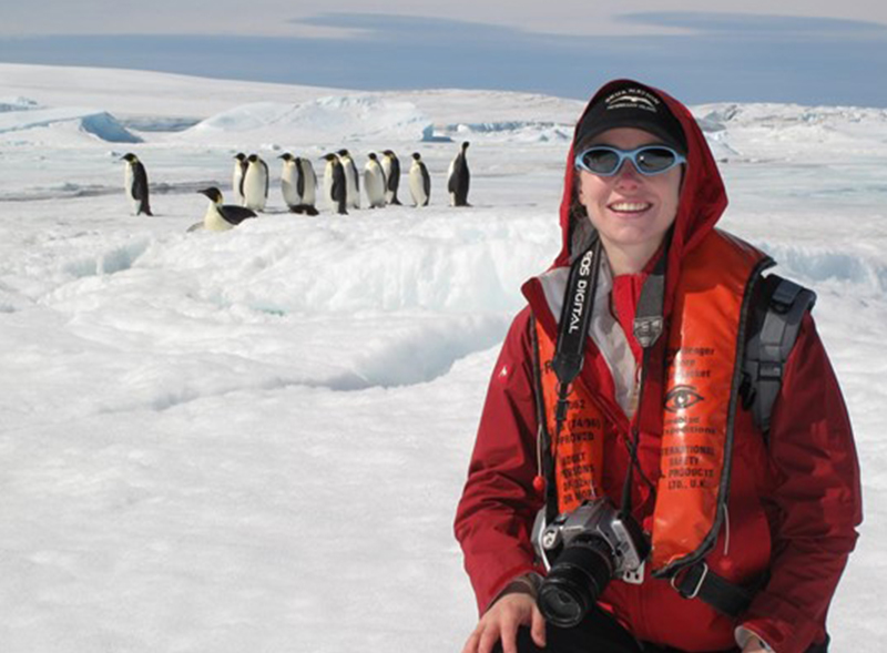 Heather standing in front of a group of penguins in a white snow field.