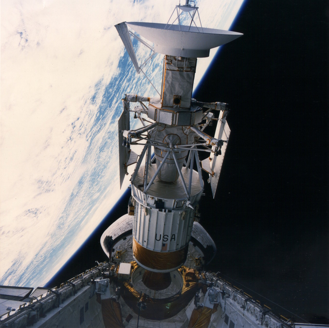 A long cylindrical spacecraft with an antenna dish on one end emerges from the cargo bay of the Space Shuttle.
