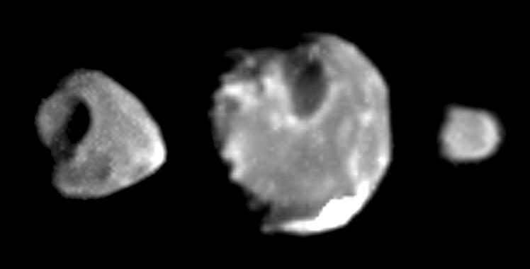 Against a black backgrouond, three moons looking like misshapened rocks of medium, large, and small size fill the screen from left to right.