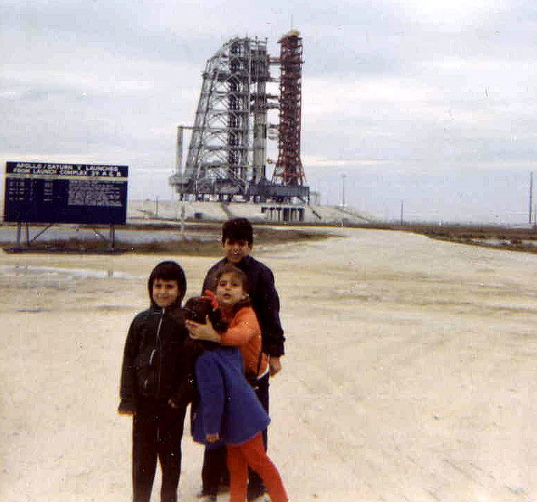 Picture of four children in front of launchpad with Apollo Saturn V rocket on it.