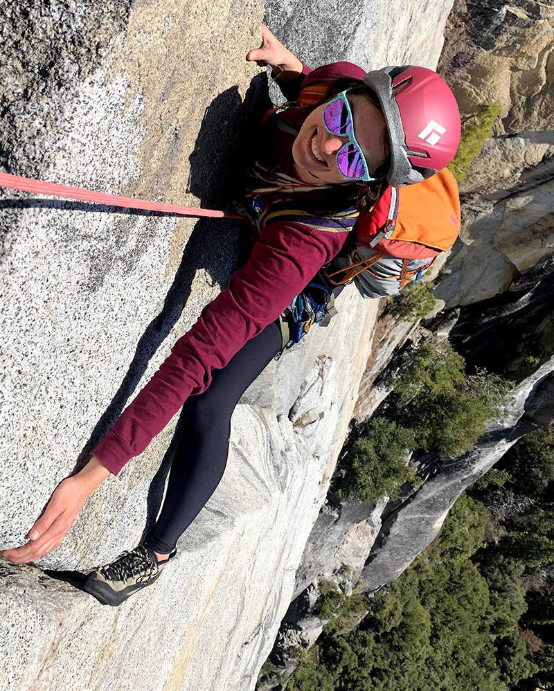 Shannon Berger smiles in her climbing gear high up on a sheer rock wall.