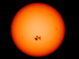 An orange, spherical Sun. Toward the middle is a large cluster of black splotches.