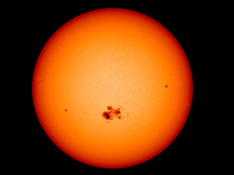 An orange, spherical Sun. Toward the middle is a large cluster of black splotches.