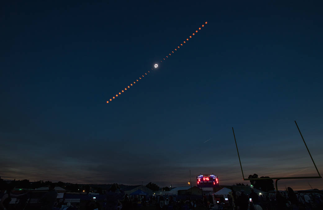 The night sky over a city, showing the progression of a solar eclipse in a line across the sky, with totality in the middle of the line