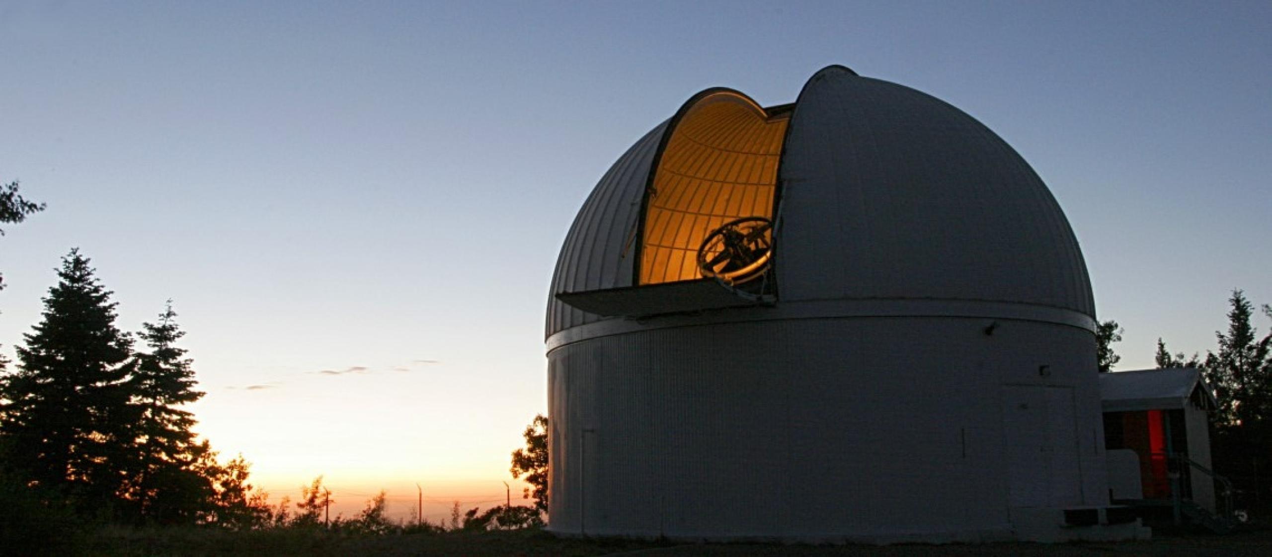 One of the telescopes used in the Catalina Sky Survey. The sun sets behind the telescope dome, which is open.