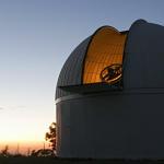 One of the telescopes used in the Catalina Sky Survey. The sun sets behind the telescope dome, which is open.