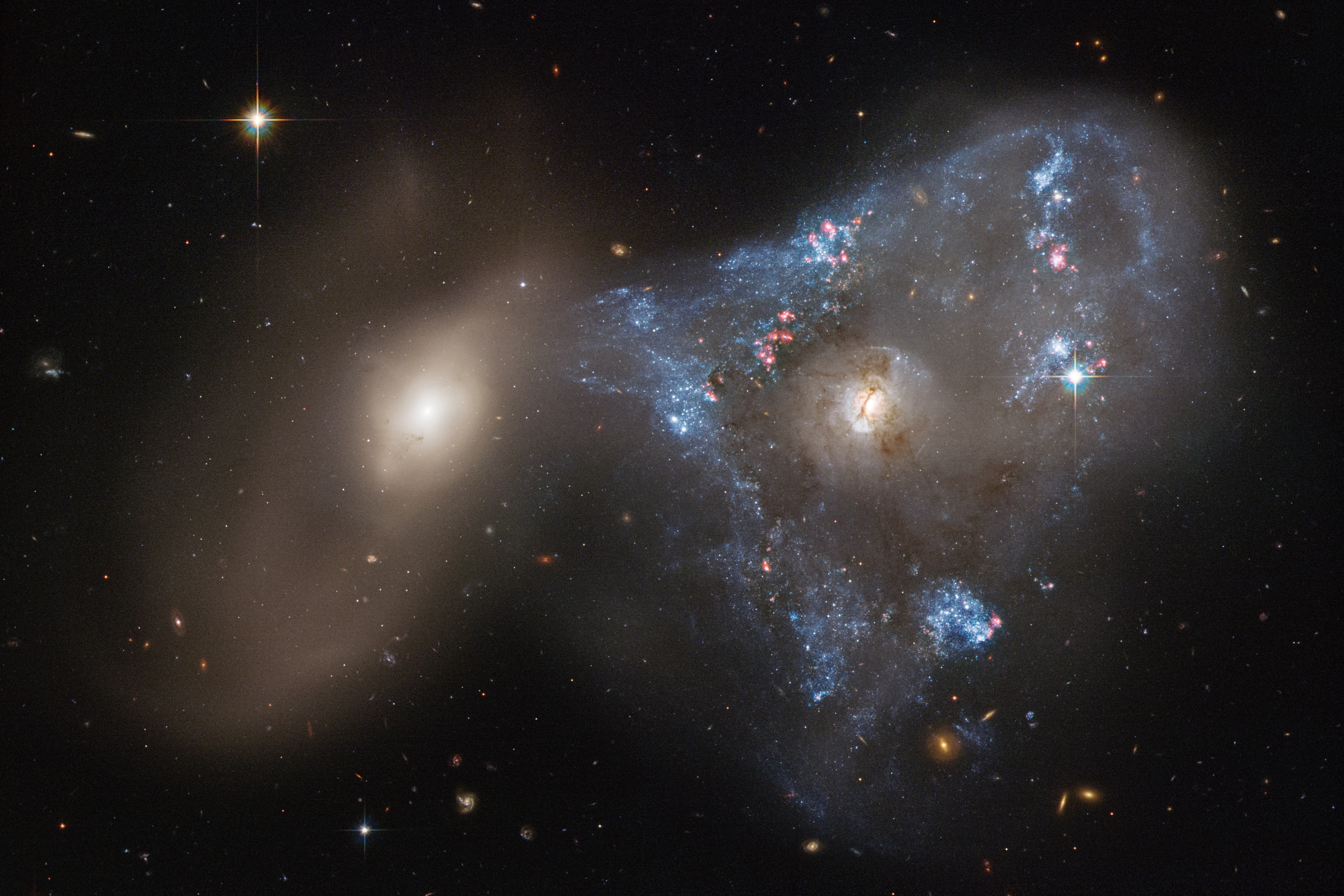 Two galaxies one right one on the left. right galaxy has a blue-white triangular star forming region surrounding it.