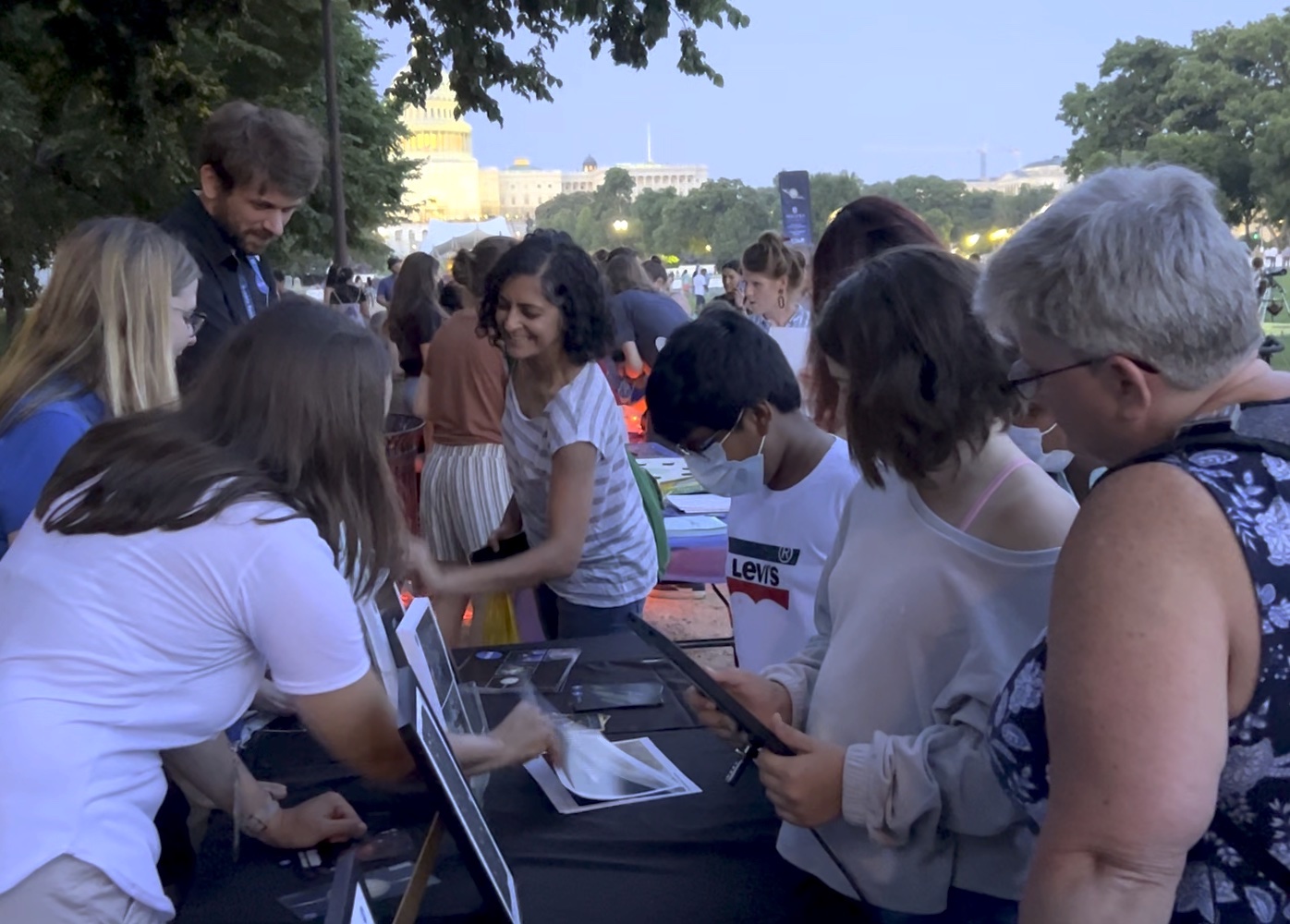 A crowd of people with members young and old cluster around a table with Hubble images.