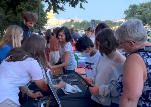 A crowd of people with members young and old cluster around a table with Hubble images.