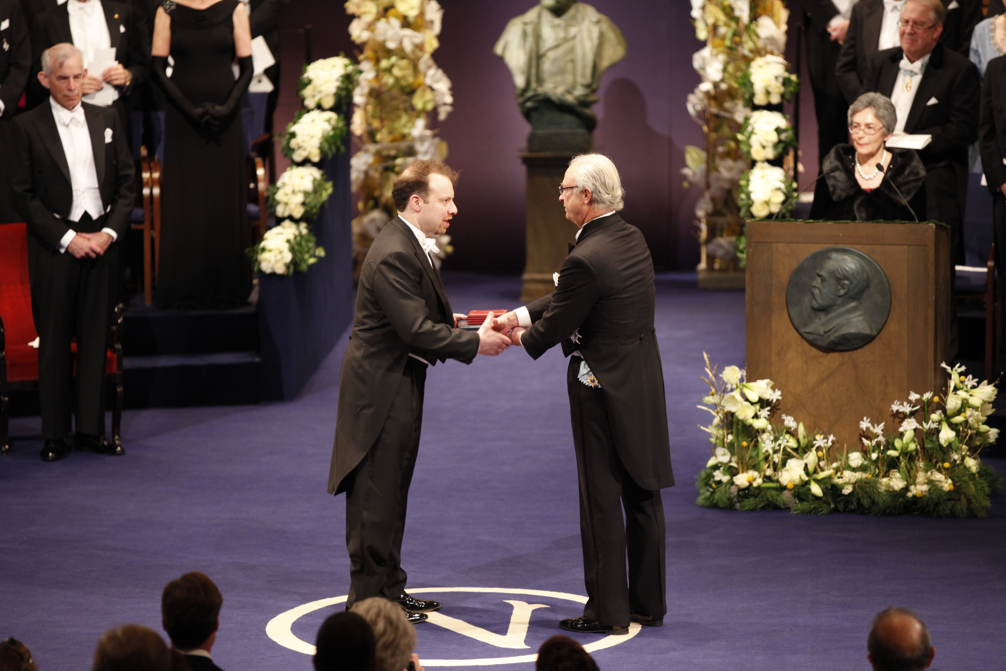 Astronomer Adam Riess shakes hands with an official at the Nobel Prize ceremony as he receives his medal.