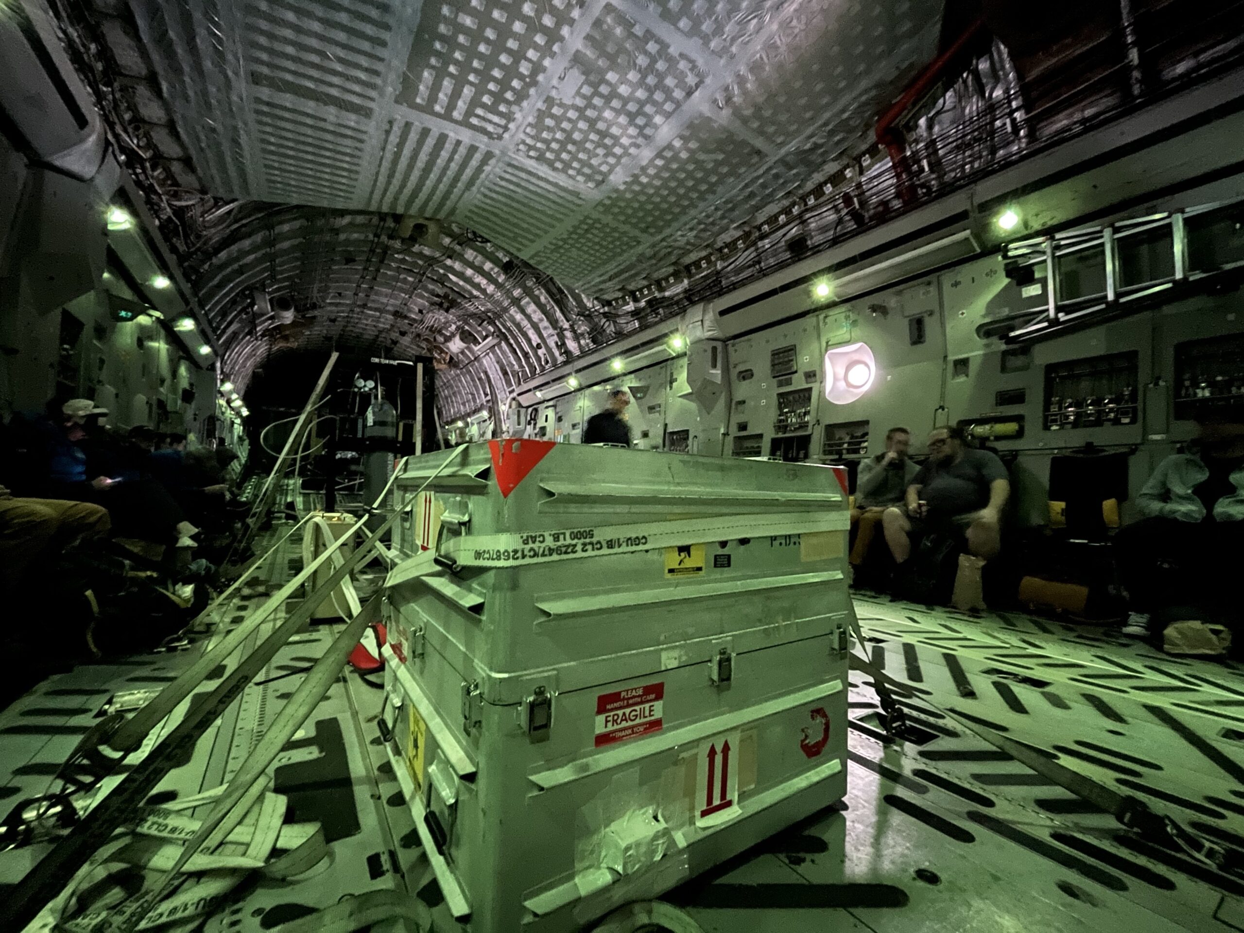 A metal box is strapped to the floor of an aircraft holding the