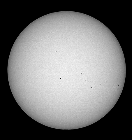 The Sun, shown as a bare orb in black and white. Some sunspots speckle the gray surface in black.