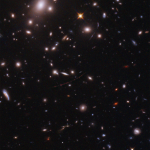 Galaxies dot a black sky. a faint red arc holds three dots. the two outer dots are a lensed star cluster, the center dot is the farthest known star, dubbed Earendel.