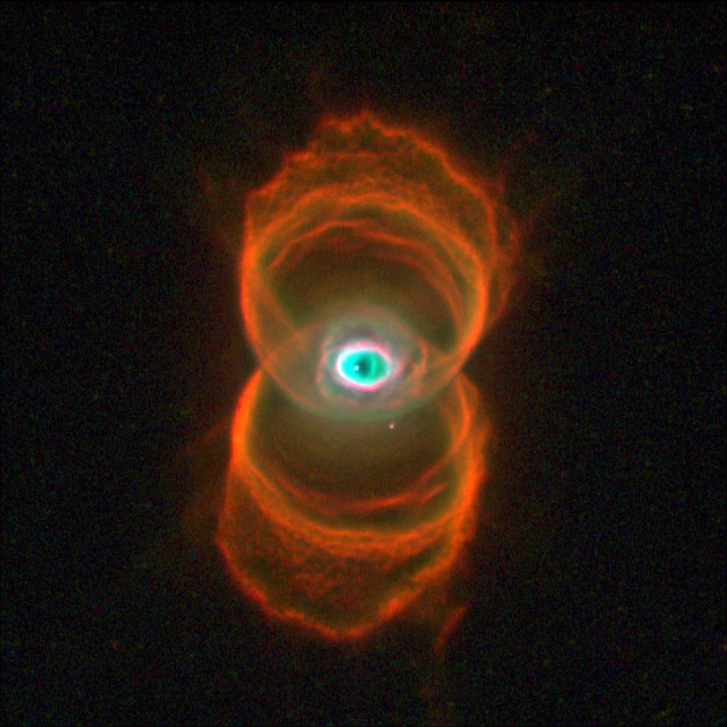 Two sets of rings in orange and gold stacked one above the other form the shape of a hourglass. At image center, where the two sets of rings overlap, is an area of white, green and black dust in a shape that is similar to the human eye.