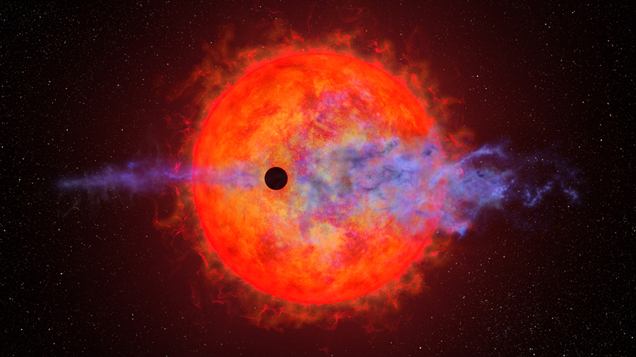 This illustration shows the ball of a red dwarf star. It is mottled with dark spots and finger-like filamentary outbursts. In front is a much smaller black circle representing the silhouette of a planet passing in front of the star. The red dwarf's furious activity is causing the planet's atmosphere to escape into space. This appears as wispy blue filaments along the planet’s straight horizontal orbital path. The star is colored a rich red because it is cooler than our Sun.