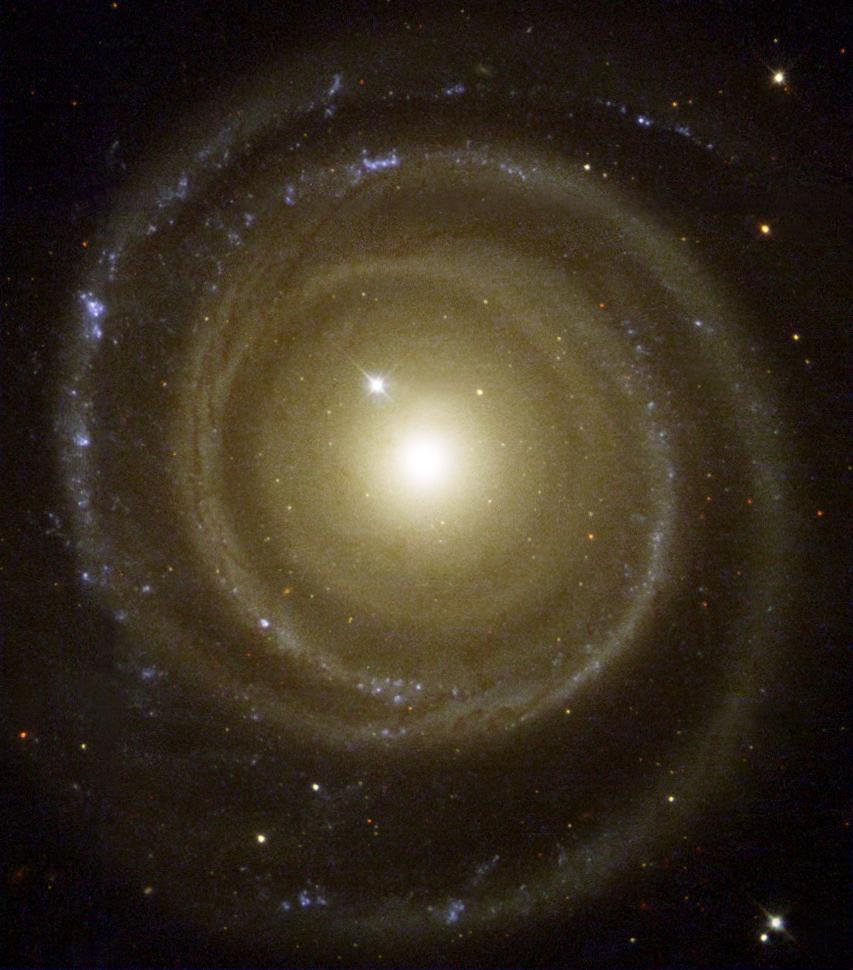 A large, face-on galaxy. It has a bright-white center with yellowish spiral arms. The spiral arm form concentric circles near the galaxy's core and curve outward further away from the galaxy.