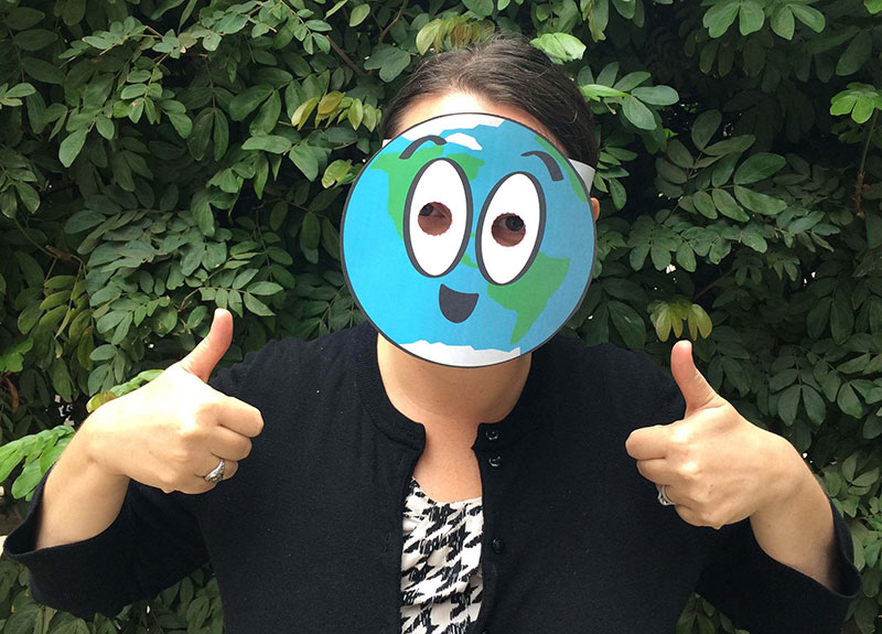 A person wearing a cartoon paper mask of the Earth gives two thumbs up.