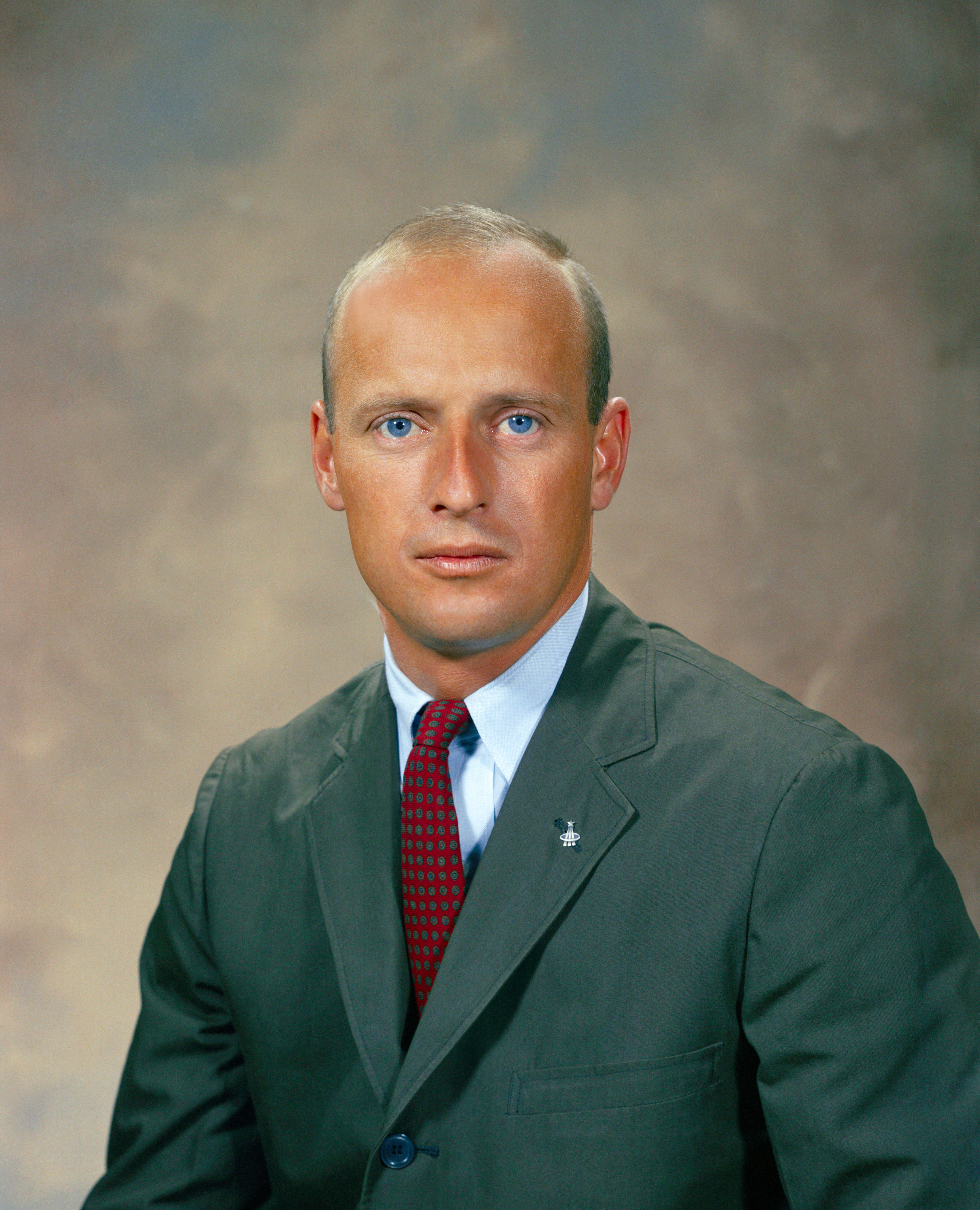 Headshot of a man in a green jacket and red tie