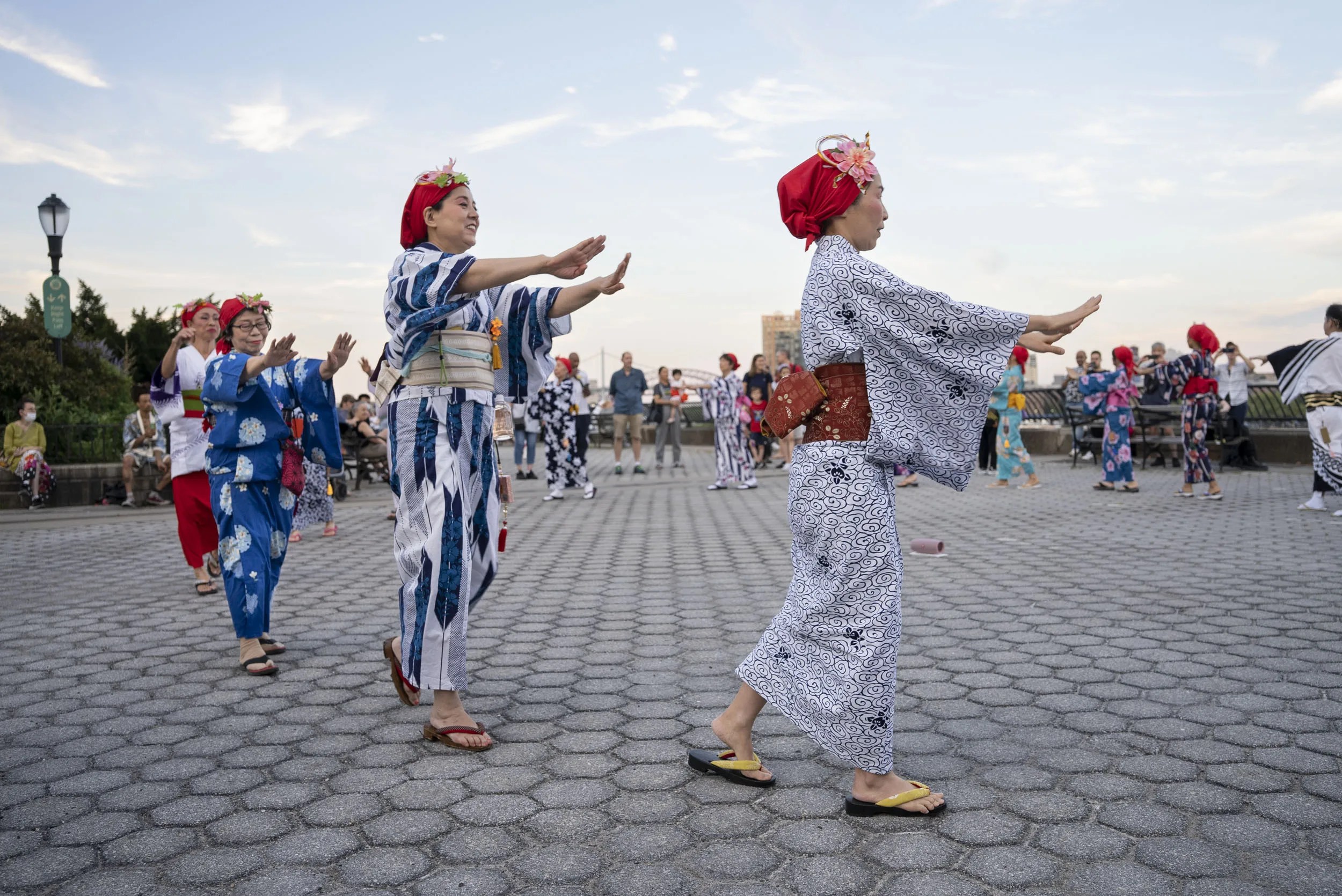 Many women dancing outside in traditional Japanese attire including kimonos and red headwear with flowers