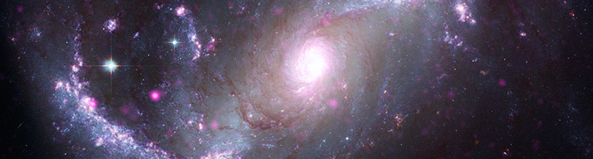 NGC 1672. Shown face on, this spiral galaxy has two major arms curving away from the bright swirling light at its core. One arm extends to our lower left with a gentle upward curve. The other extends to our upper right with a curve reminiscent of a question mark. Both arms have a cloudy, silver blue quality, and are dotted with bright white and purple stars of varying sizes. In this galaxy, categorized as a "barred" spiral, the arms don’t appear to reach the bright core. The space around the bright pinkish core is a swirl of murky, pale silver cloud.