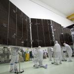 Five engineers in cleanroom suits inspect the Juno spacecraft's massive solar panels before launch.