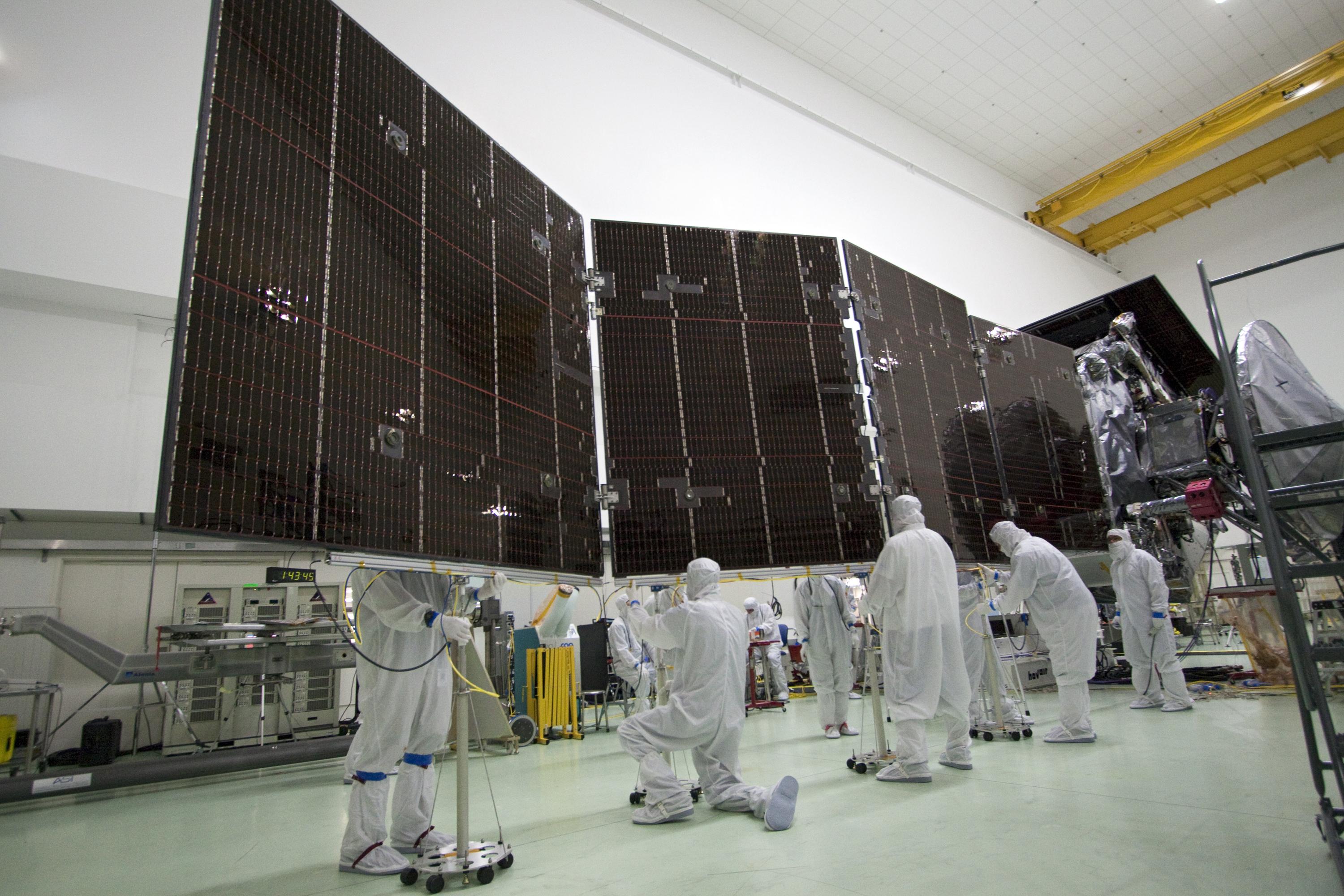 Five engineers in cleanroom suits inspect the Juno spacecraft's massive solar panels before launch.