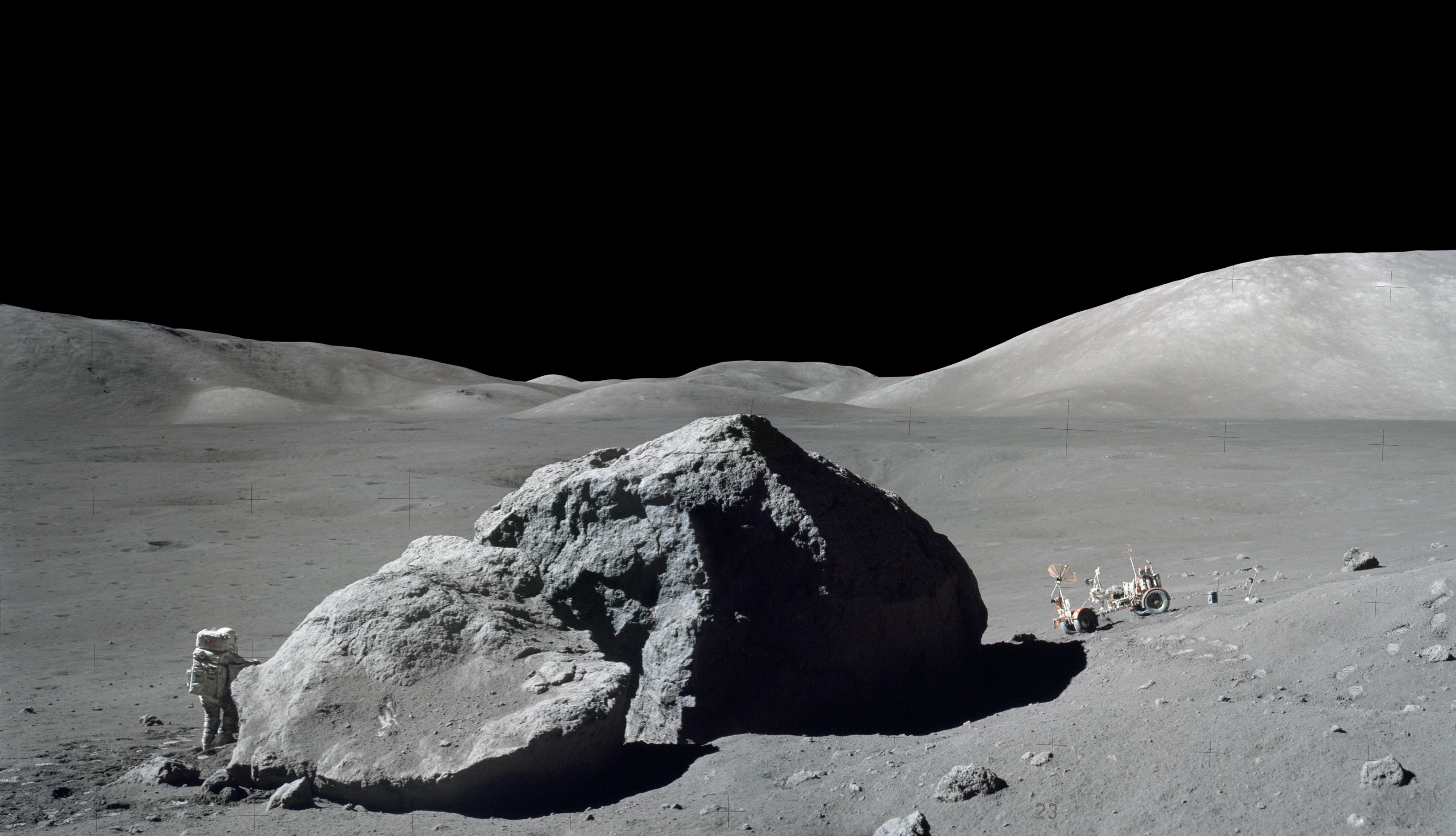Astronaut and rover on the Moon's surface, separated by a boulder several times taller than the man. 
