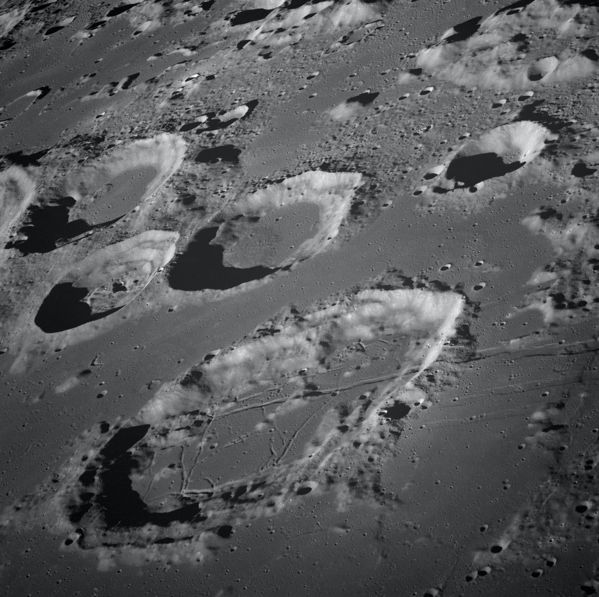 Craters on the Moon, seen from a low oblique angle. The floor of a large foreground crater has fracture-like patterns.