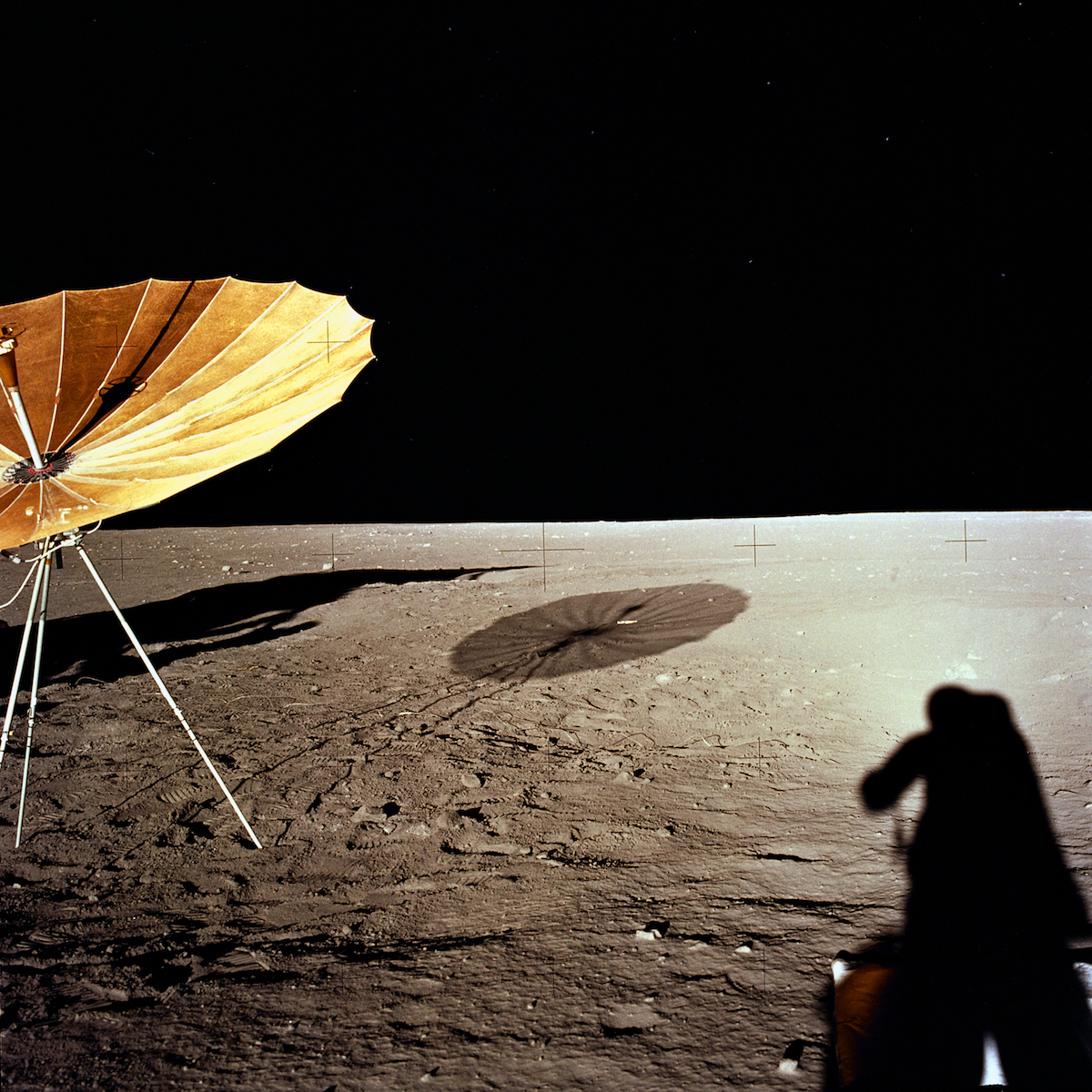 an antenna deployed on the Moon's surface, resembling an inverted golden umbrella, with an astronaut's shadow in the foreground