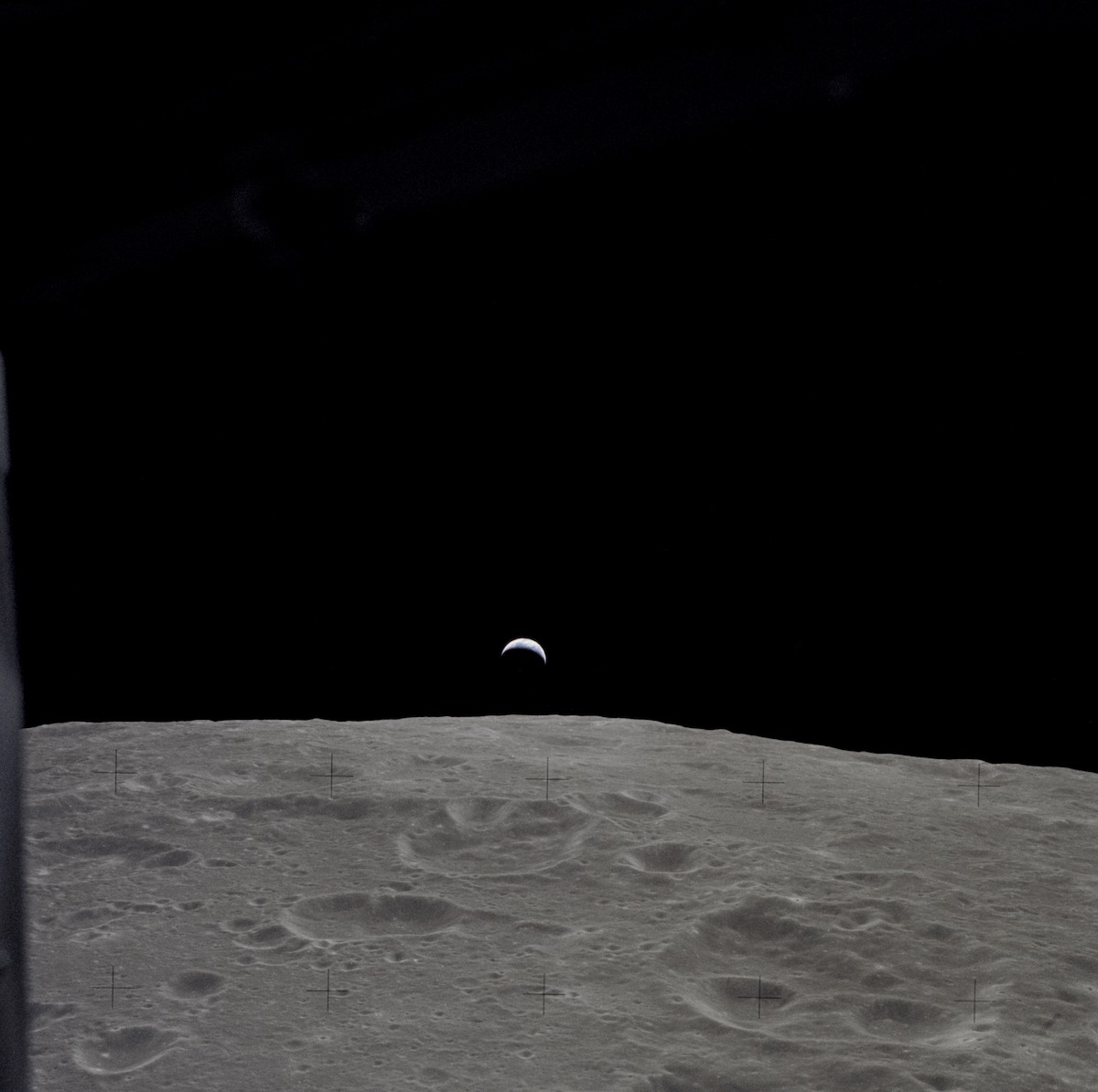 crescent Earth seen in the far distance over the lunar horizon