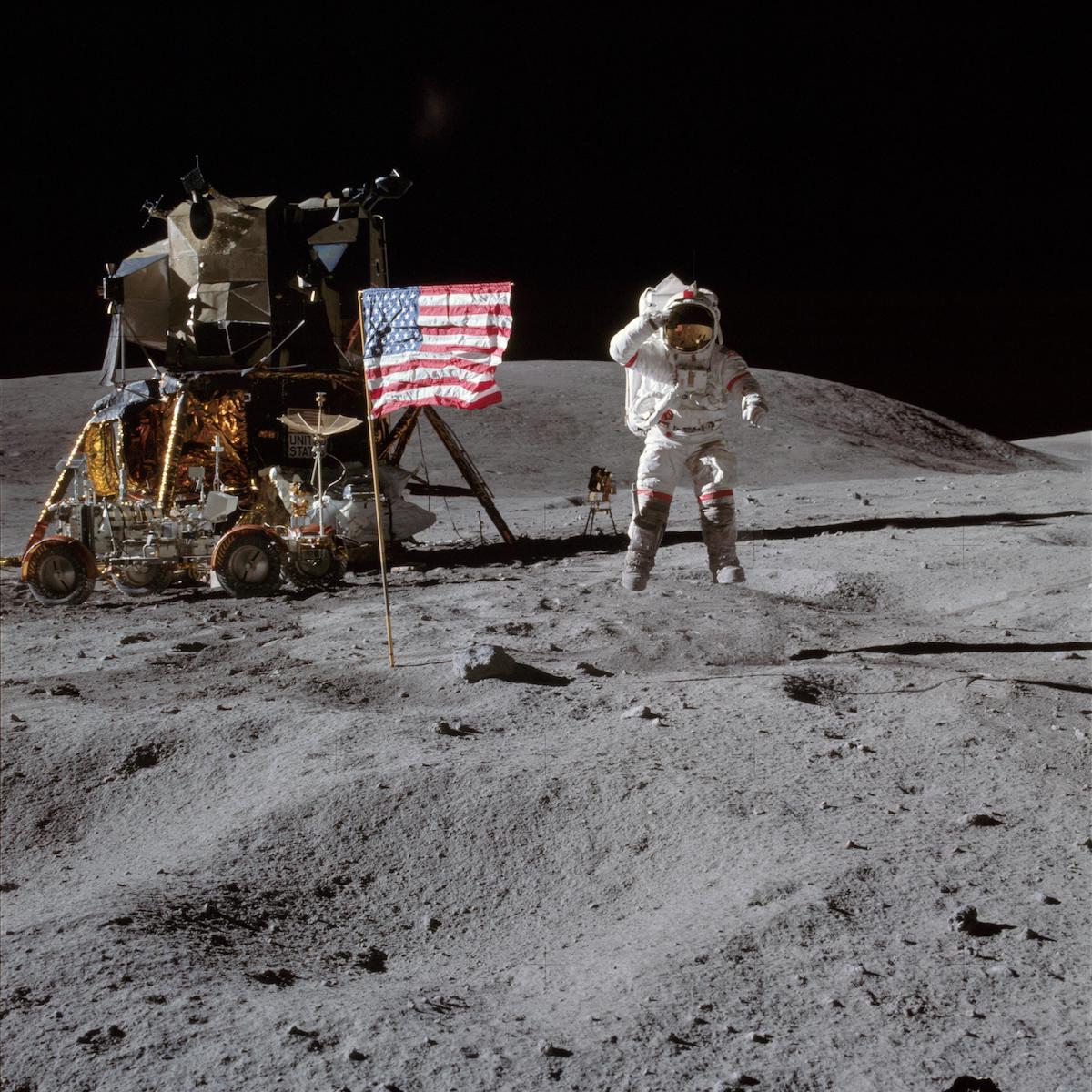 astronaut jumps and salutes near flag and lunar module