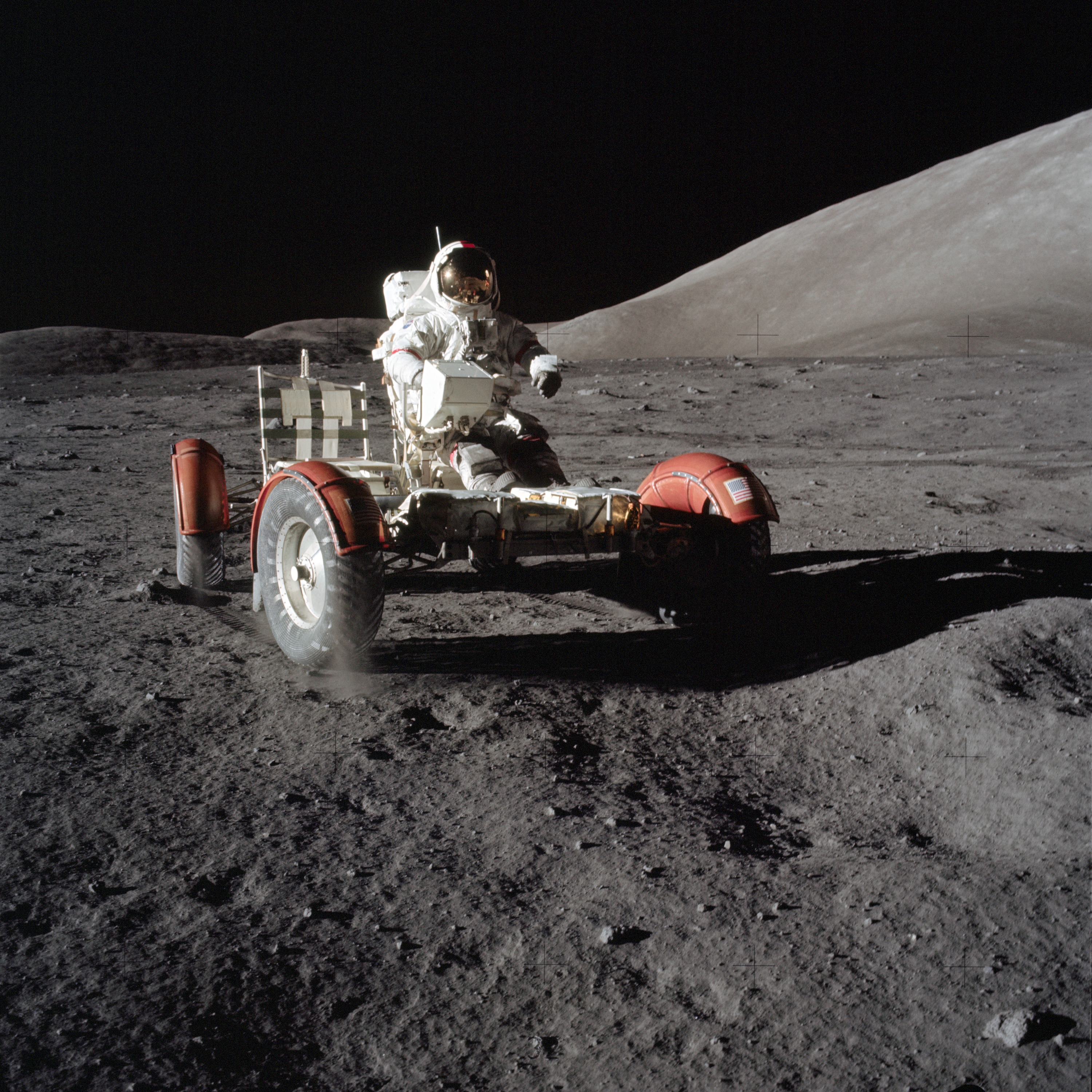 On the Moon's grey, dusty surface, an astronaut stands near a rover. A hill rises in the background under a black sky.