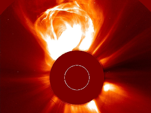 Image of a dark orange disc, the Sun, with bright white blasts emerging from it. The largest blast forms a messy loop which appears to have about the same diameter as the Sun itself.