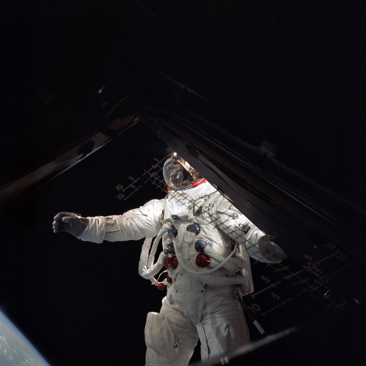 Astronaut in space, brightly lit against a black sky, seen through a spacecraft door.