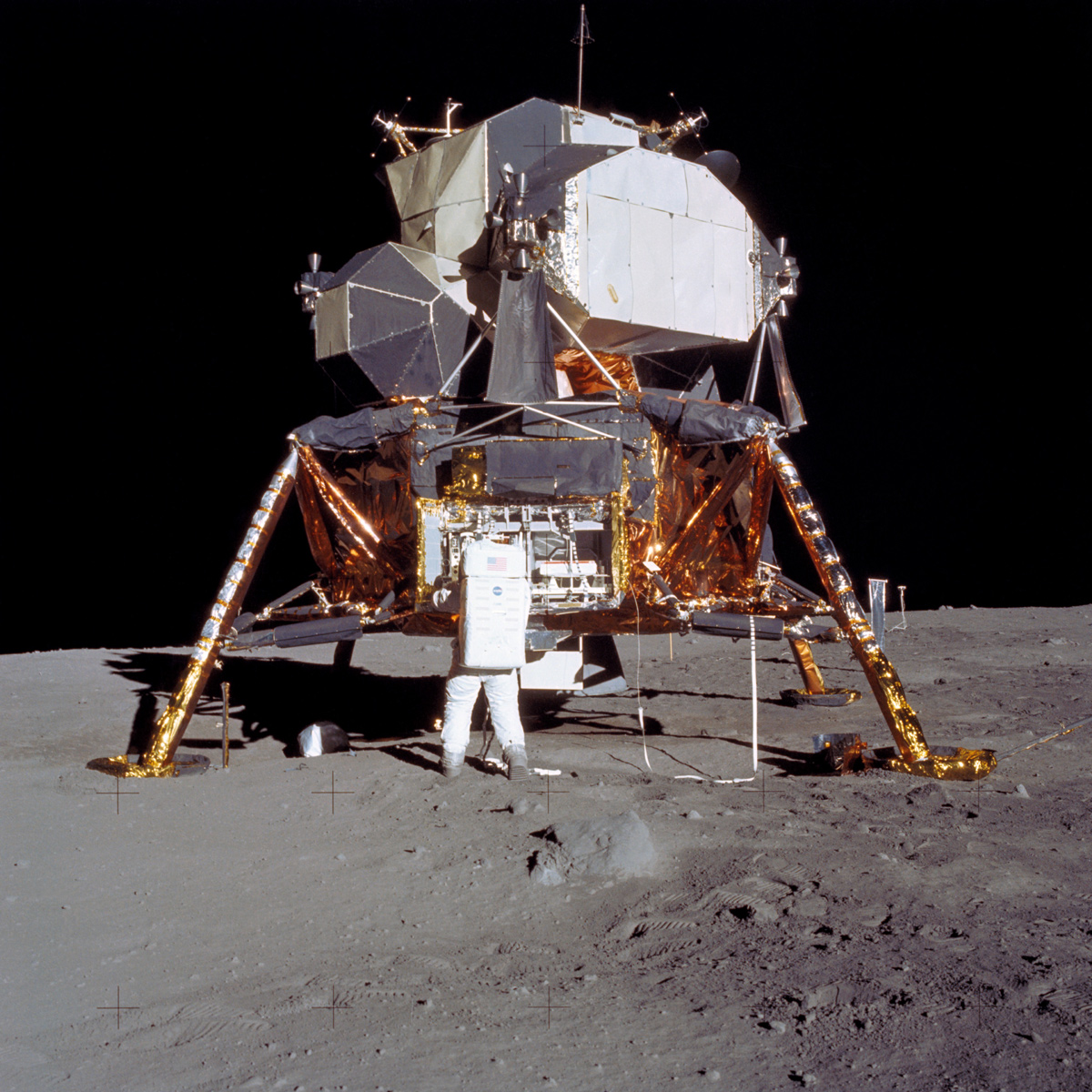 Lunar module on surface of Moon, with astronaut in foreground facing away from viewer