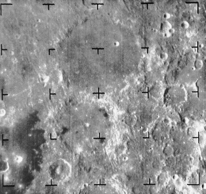 View of two large craters on the Moon, with bright patches on their edges and a dark patch near bottom left. 
