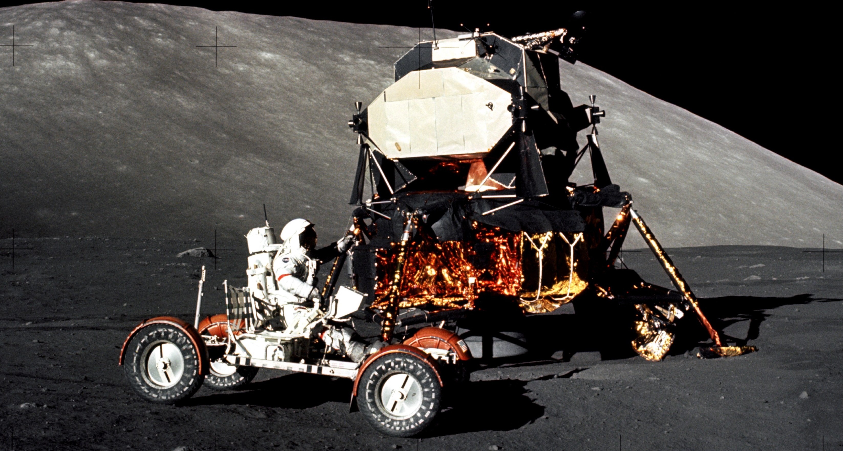 Man in moon buggy on the Moon, with a large hill blocking most of the horizon. 