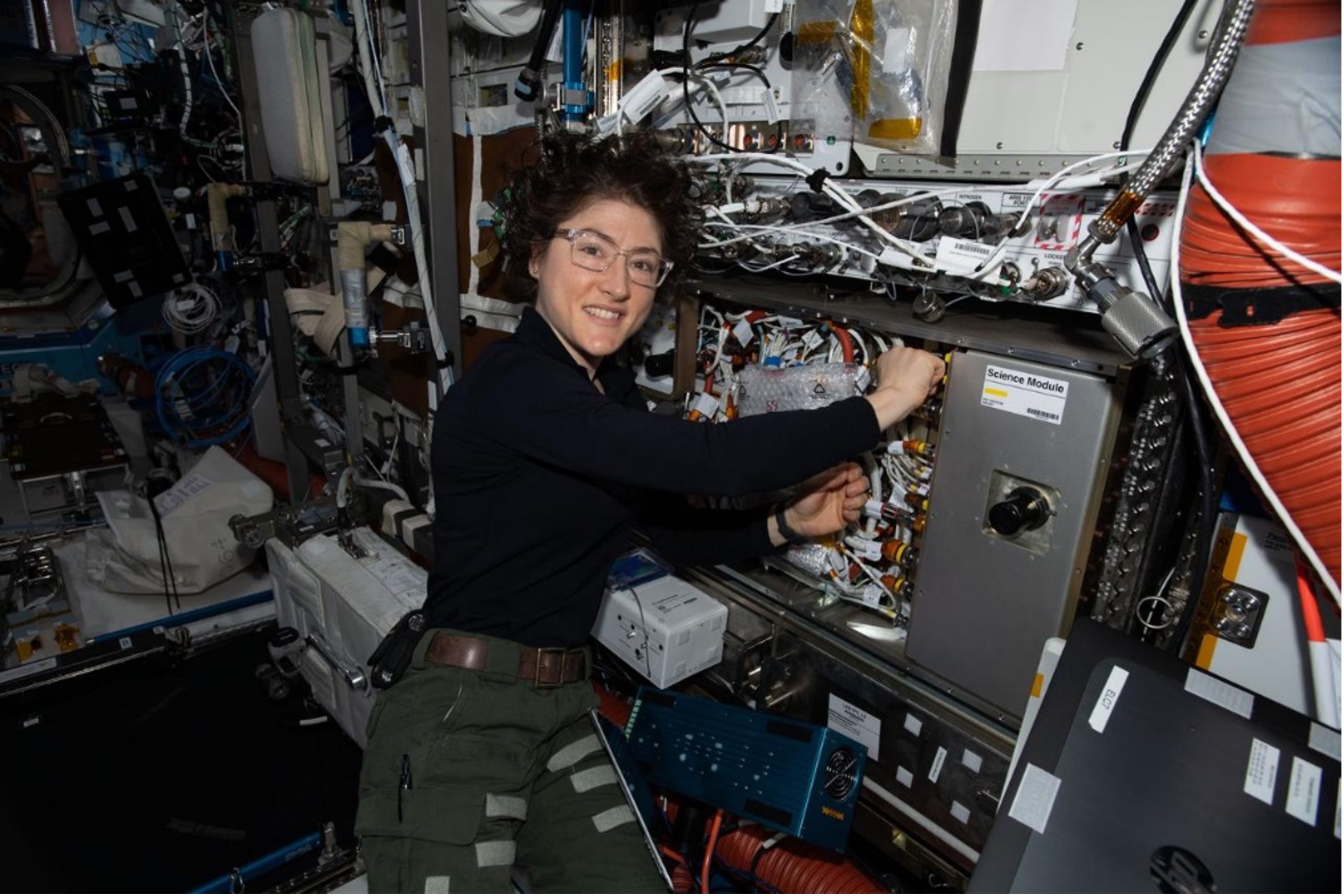 A photo of astronaut Christina Kock wearing glasses onboard the International Space Station as she works on hardware for the Cold Atom Lab.