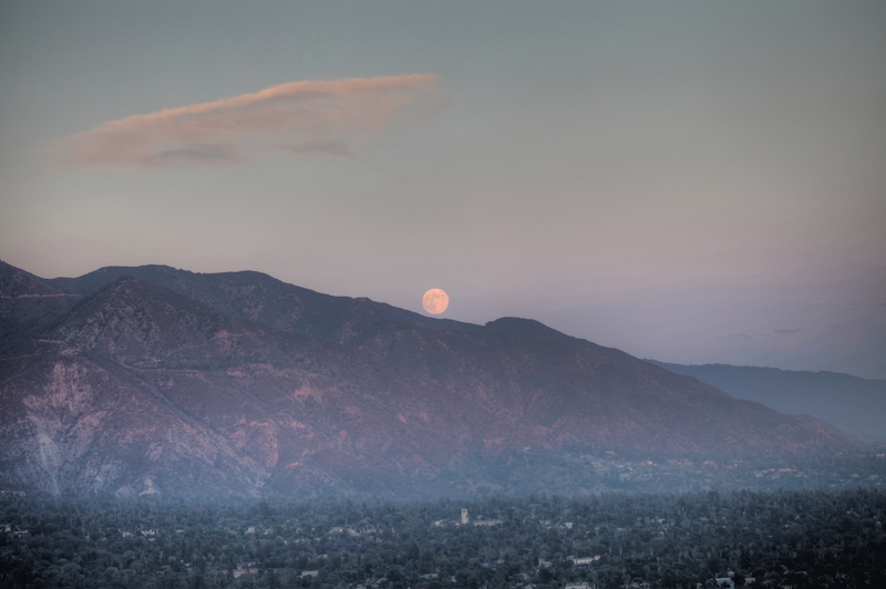 Moon rising over mountains in a hazy, twilit atmosphere. 